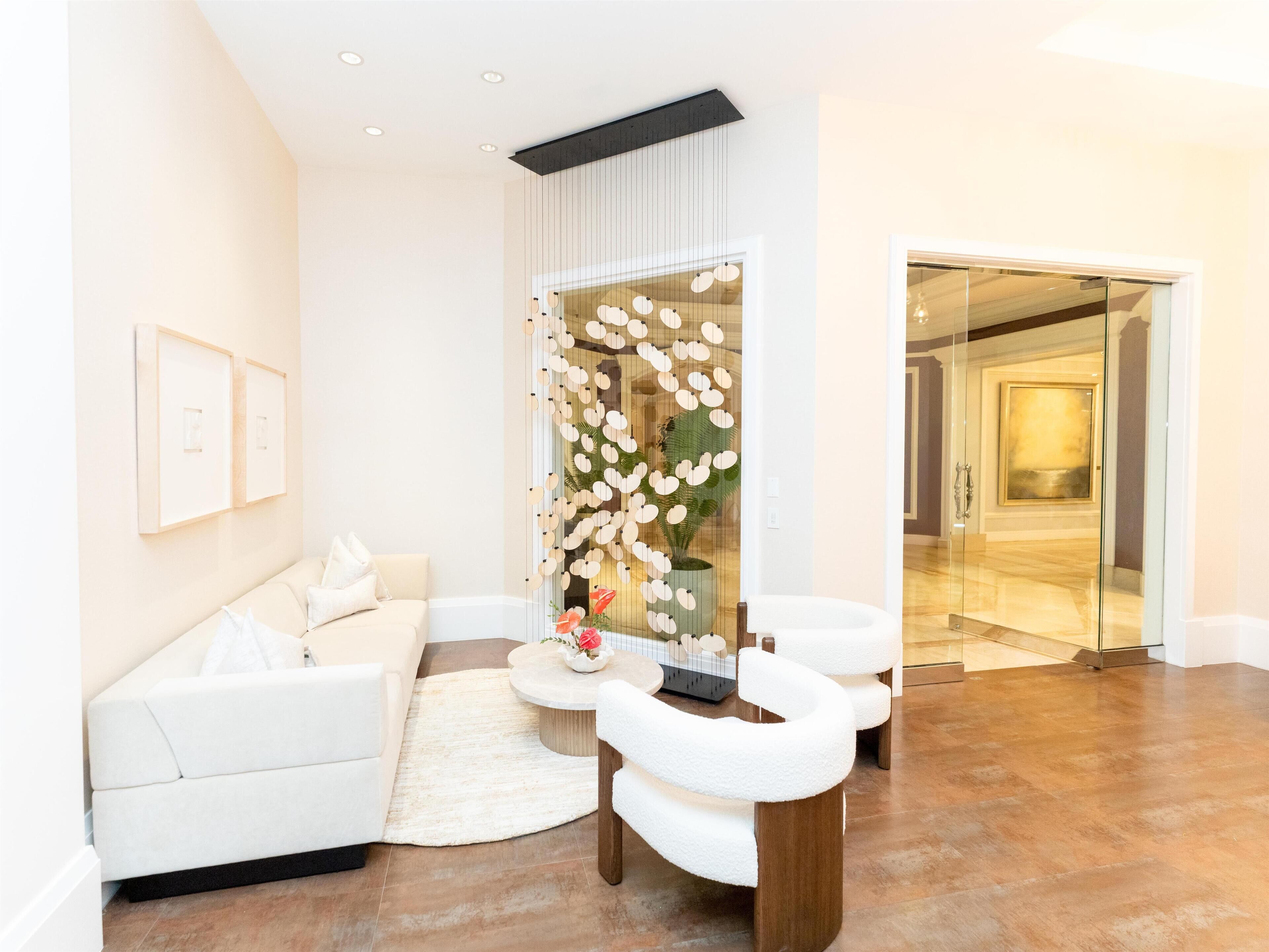 A modern living room with a white sofa, a round coffee table, and a white armchair. There is a decorative wall with hanging lights and a plant.