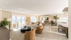 A spacious living room with a sofa, armchairs, a coffee table, and a dining area with a table and chairs. There are potted plants and a large window offering a view. - Eau Resort & Spa (Manalapan)