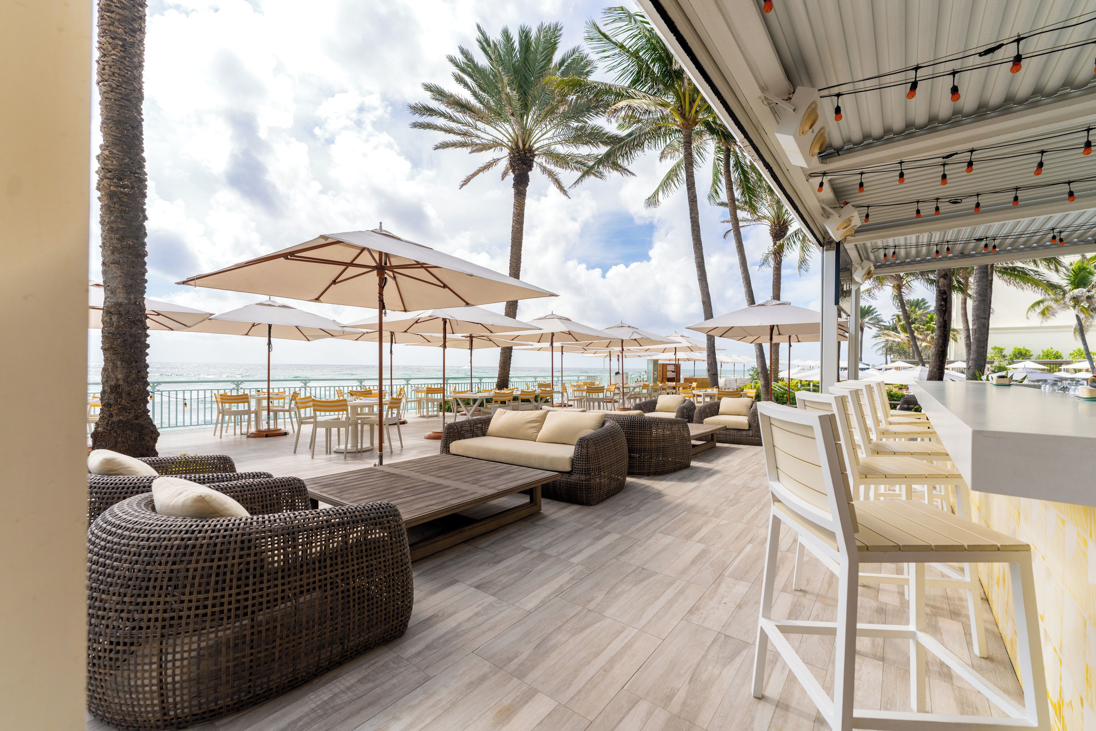 A beachside lounge with wicker sofas, white umbrellas, and a bar area.