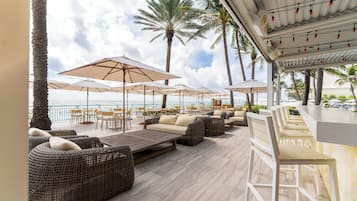 A beachside lounge with wicker sofas, white umbrellas, and a bar area.