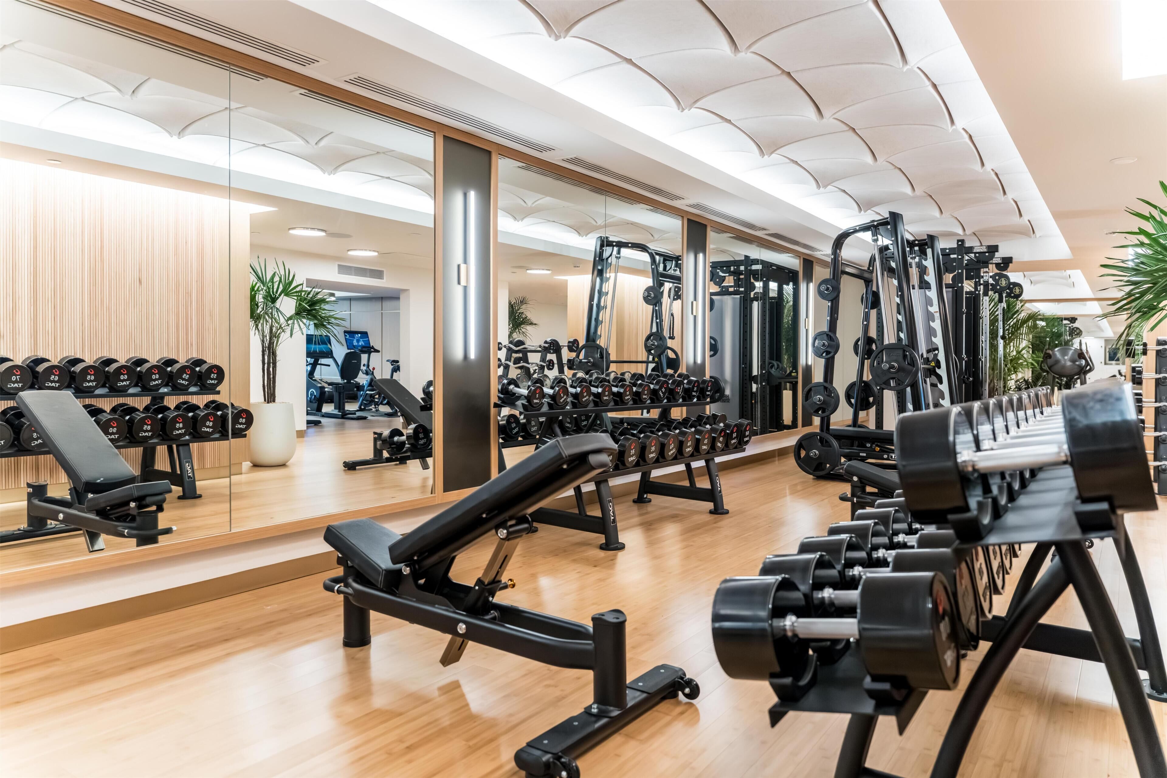 A gym with weightlifting equipment, mirrors, and a wooden floor.