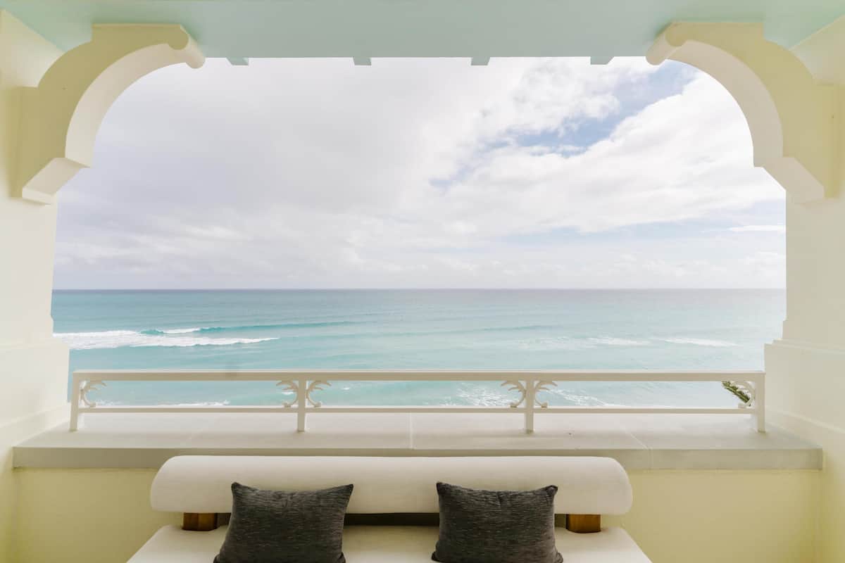Een balkon met uitzicht op de oceaan, een witte bank en twee kussens.