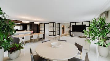 A modern living room with a round dining table, multiple seating options, and a large TV.