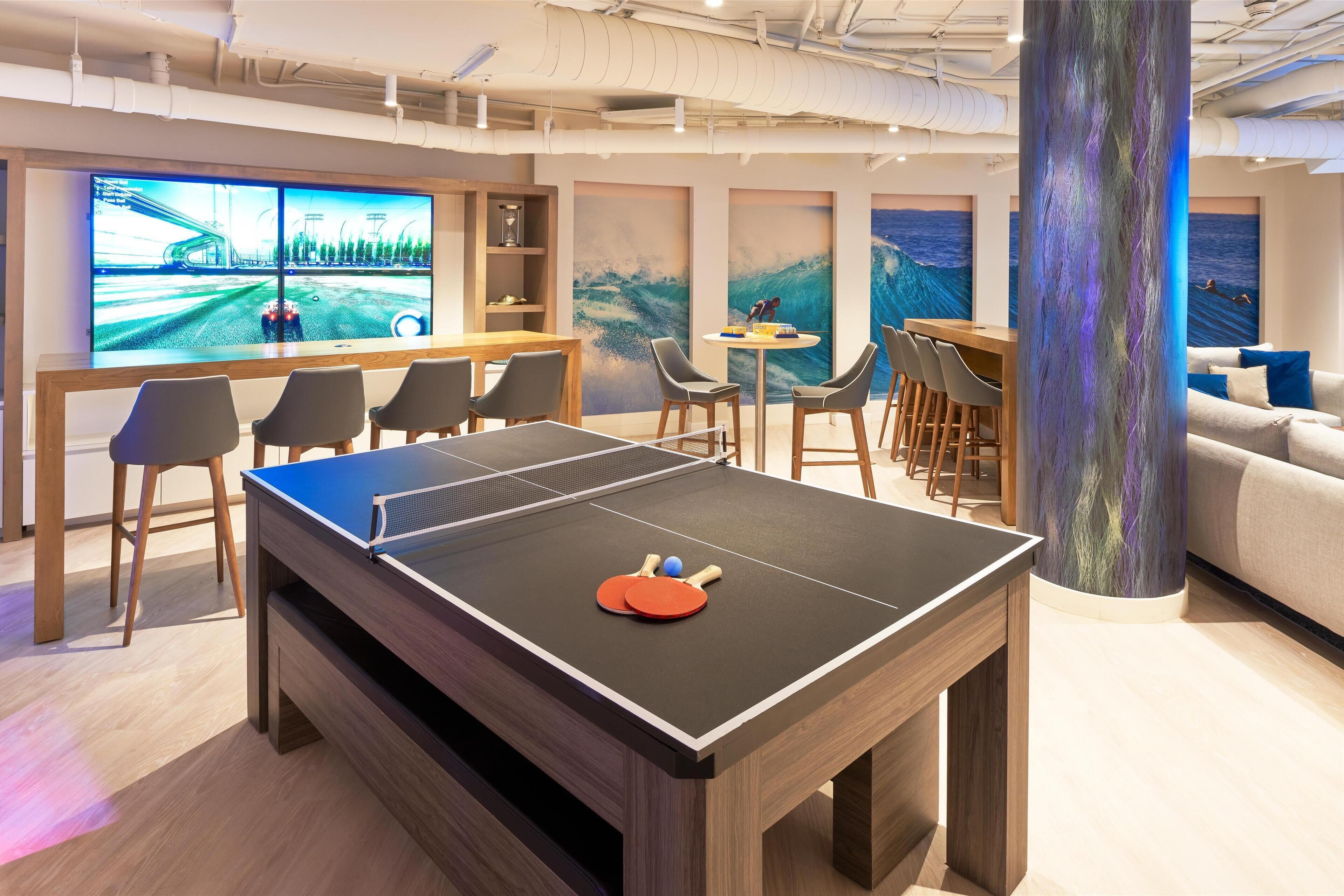 A ping pong table in a modern room with a large TV, comfortable seating, and a large column.