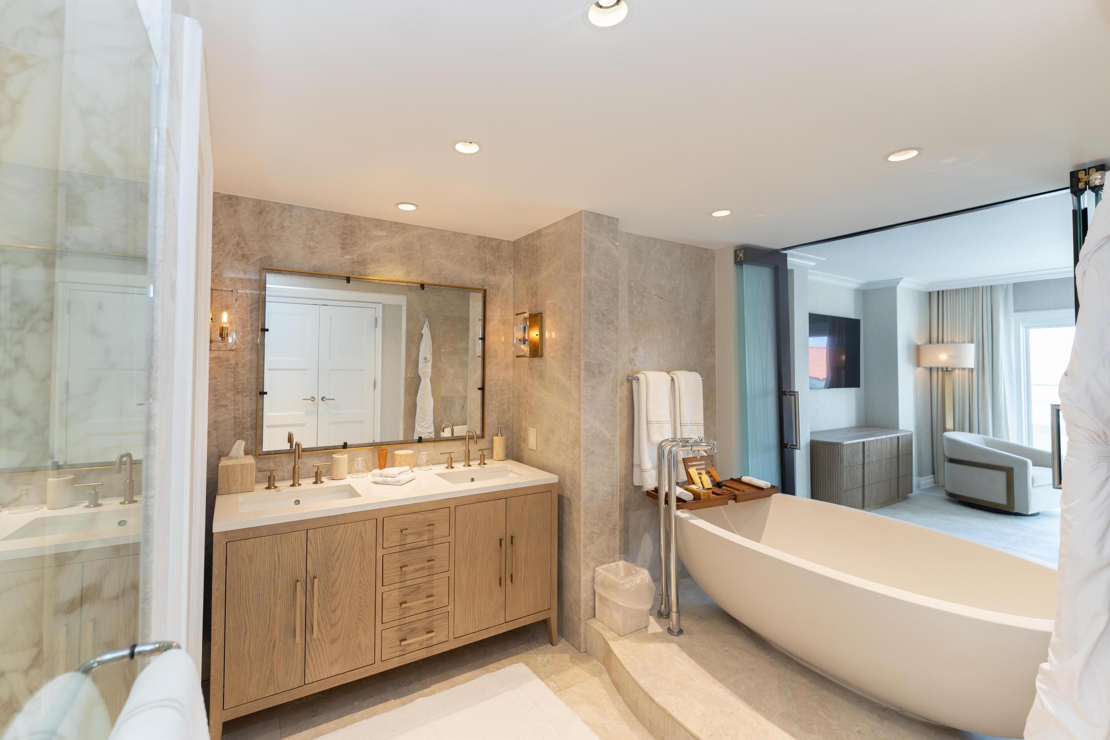 Un baño moderno con un espejo grande, dos lavamanos, una bañera y muebles de madera.