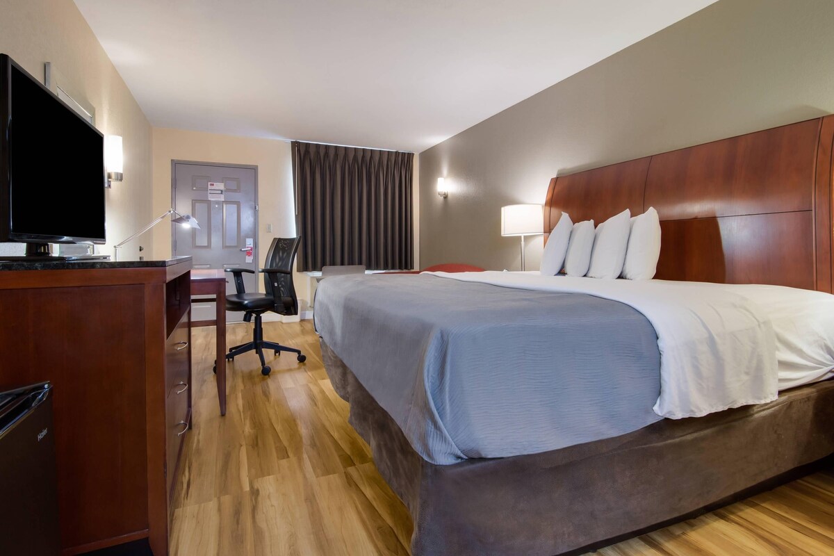 A hotel room with a large bed, a desk with a television, and a chair.