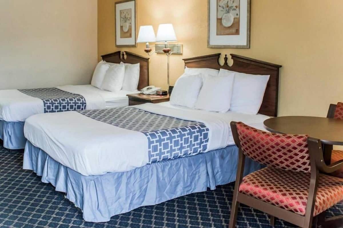 A hotel room with two beds, a desk, a chair, two bedside lamps, and artwork on the walls.