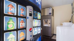 Una máquina expendedora con diversas opciones de bebidas, una cafetera y una lavadora en una habitación.