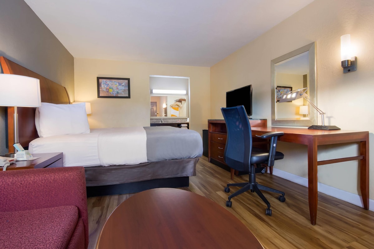 A hotel room with a bed, desk, chair, and a small table.