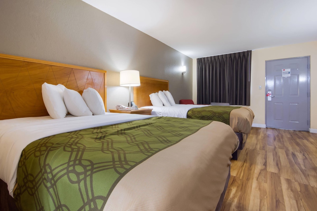 A hotel room with two beds, wooden headboards, a nightstand with a lamp, a red chair, and a door with a sign.