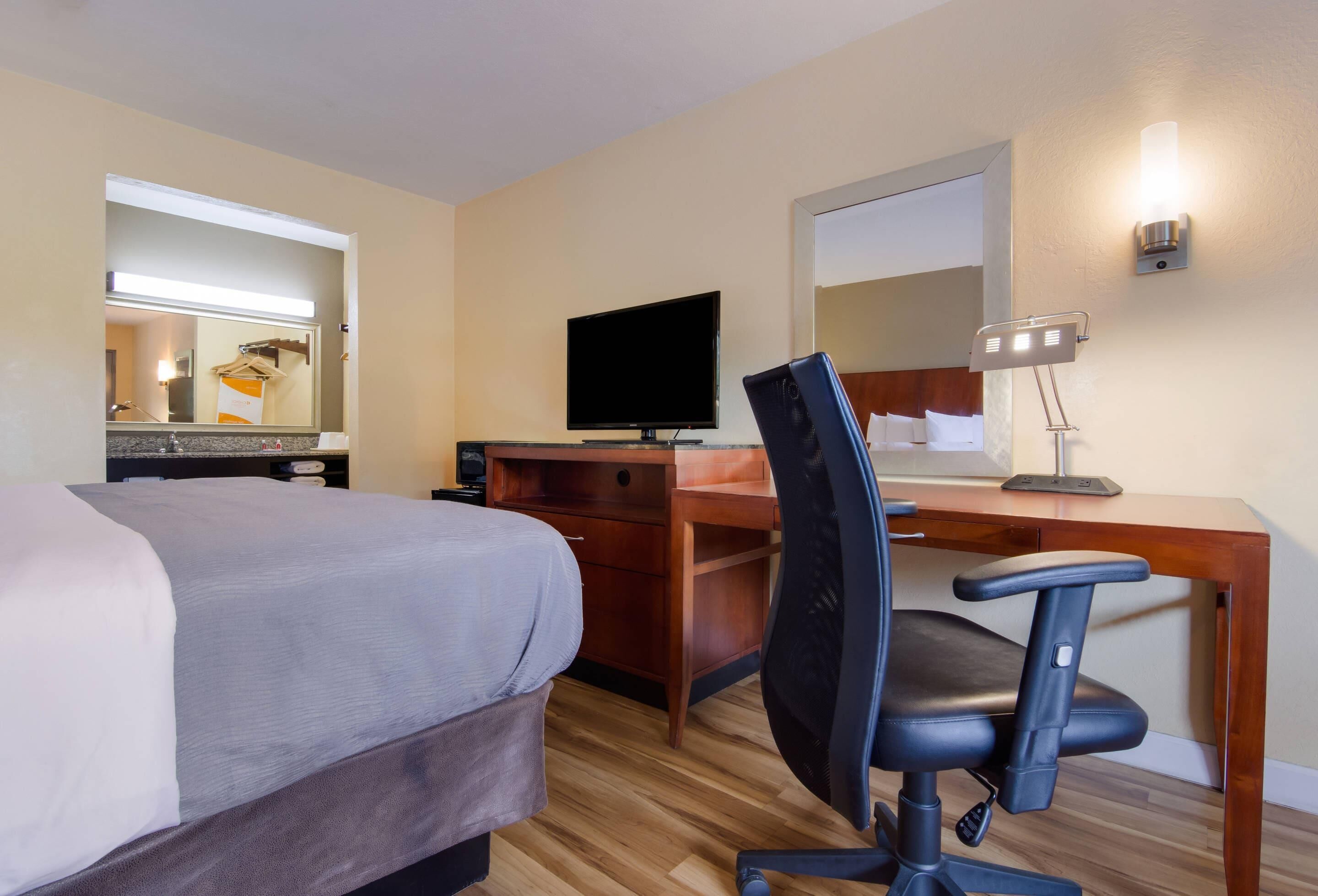 A hotel room with a bed, desk, chair, television, and a mirror.