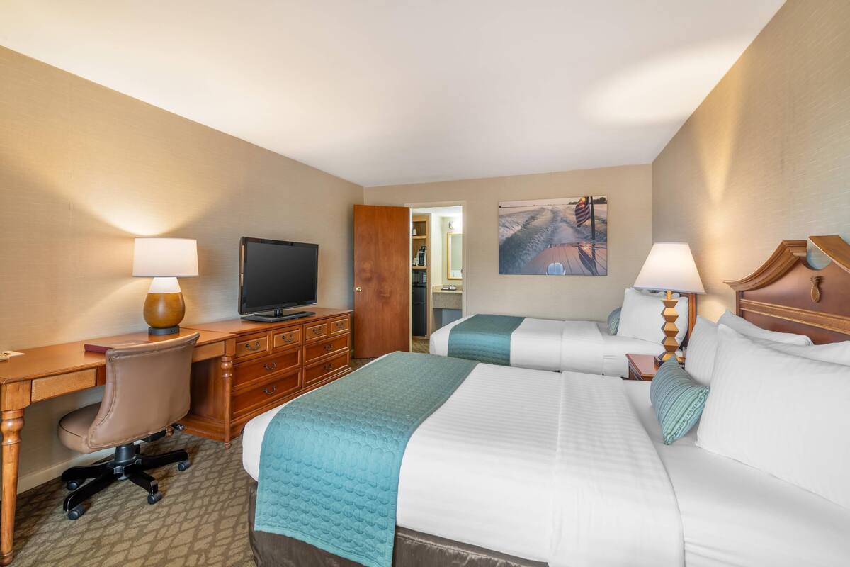 A hotel room with two beds, a desk, a chair, a television, and a painting on the wall.