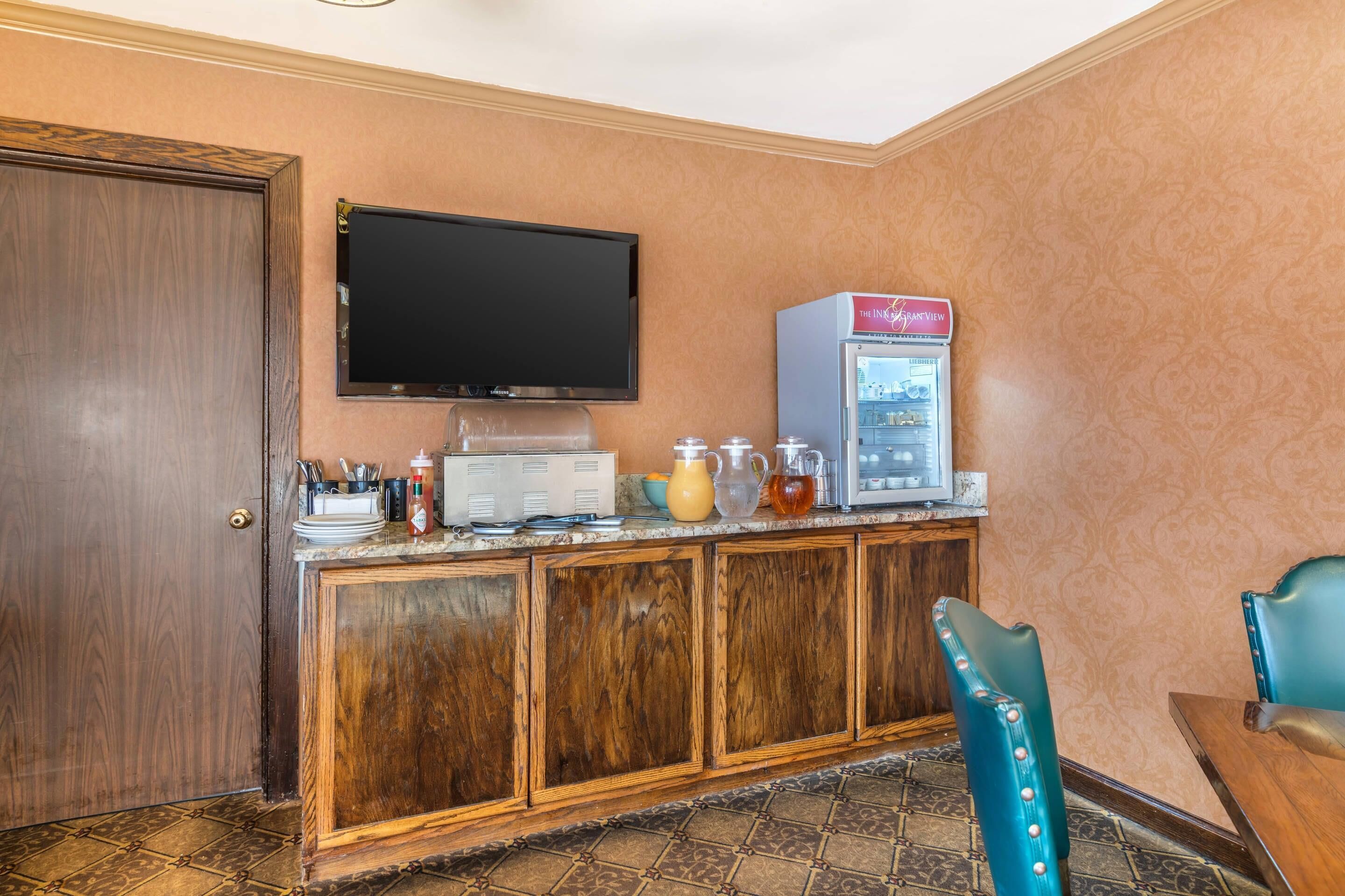 Een hotelkamer met een houten kast, een televisie, een minibar en een teal-kleurige stoel.