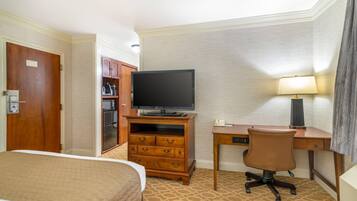 Une chambre d’hôtel comprenant un lit, un bureau avec une chaise, une télévision, une lampe et une armoire.