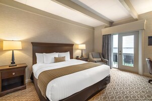 Ein Hotelzimmer mit einem großen Bett, zwei Nachttischen mit Lampen, einem Sessel und Blick durch eine Schiebetür.
