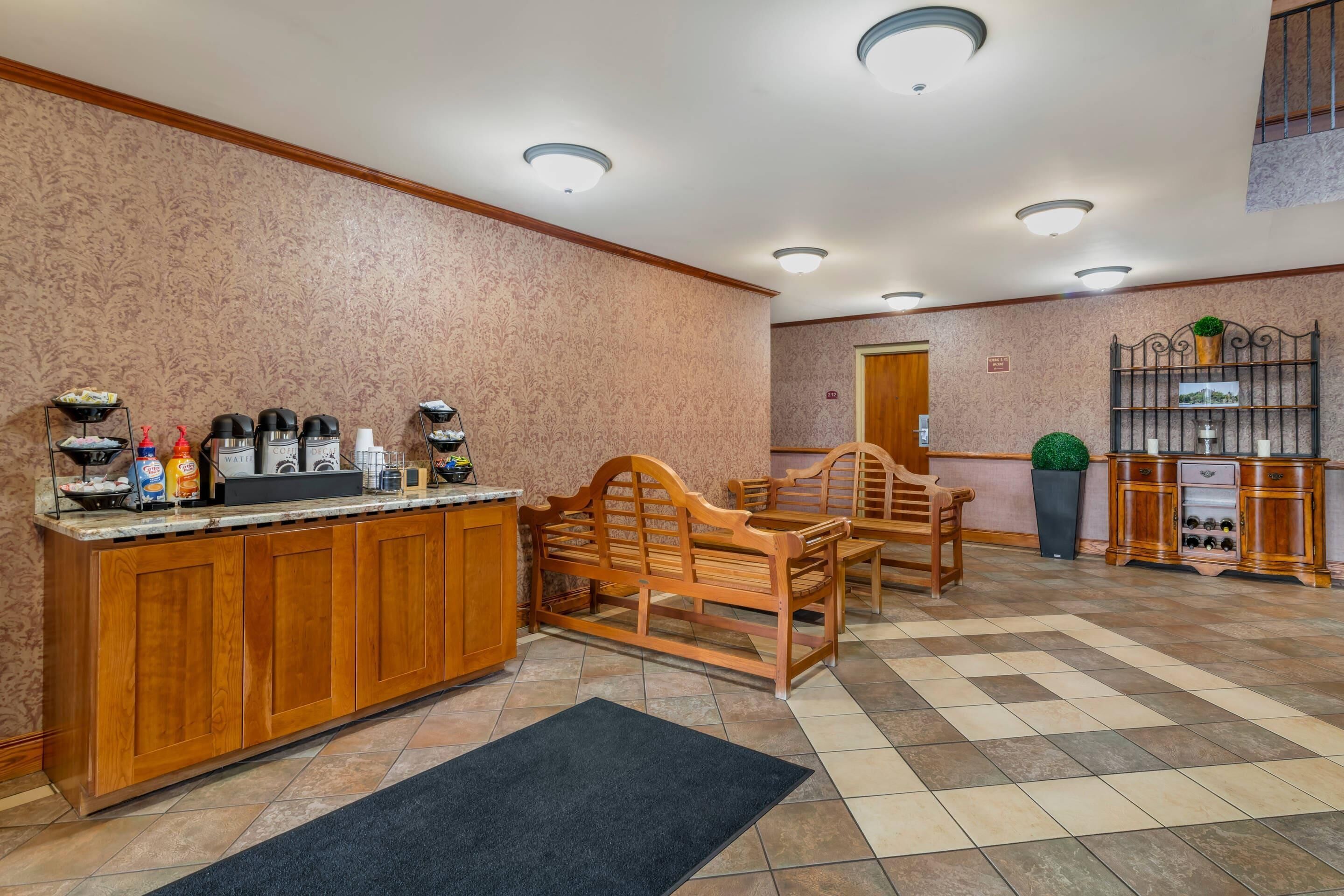 A hotel lobby with a reception desk, wooden benches, a coffee station, and a wine display.