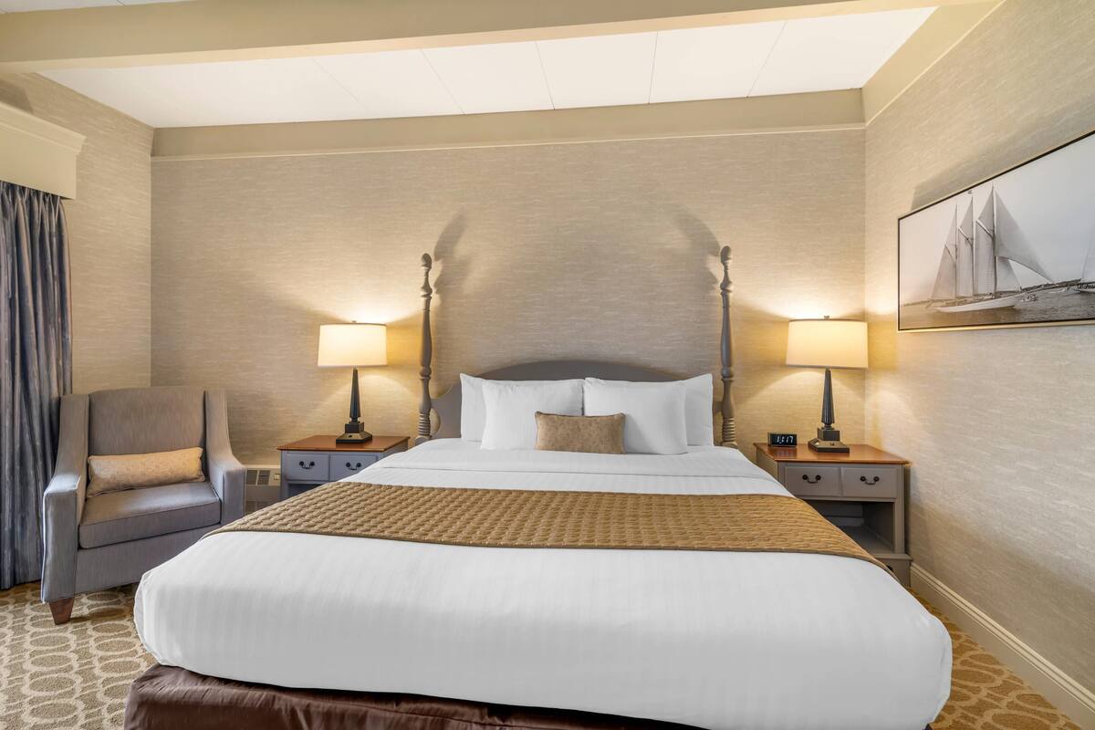 A hotel room with a large bed, two bedside tables with lamps, a chair, and a painting on the wall.