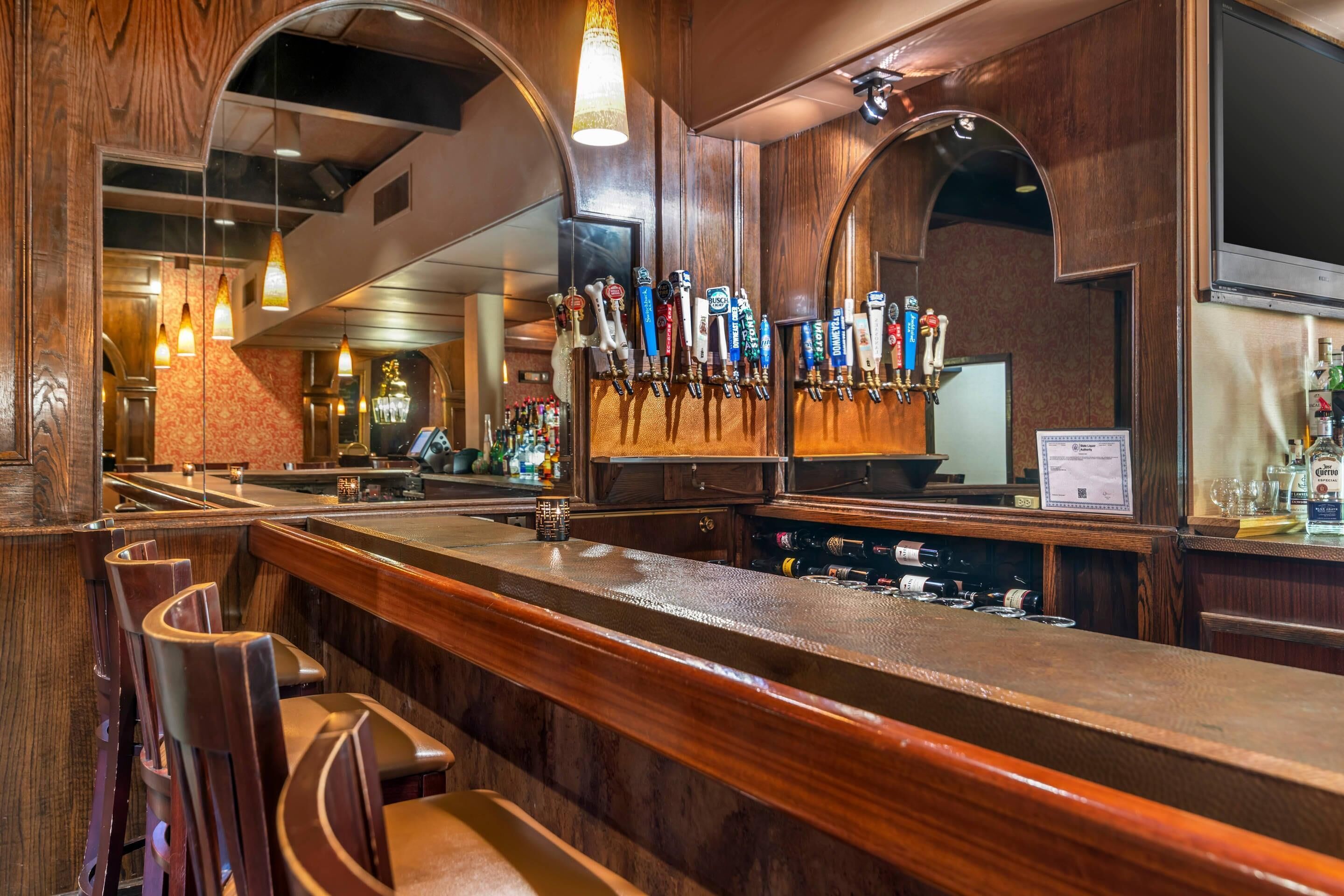 Una zona de bar con mostrador de madera, varias griferías de cerveza y taburetes.