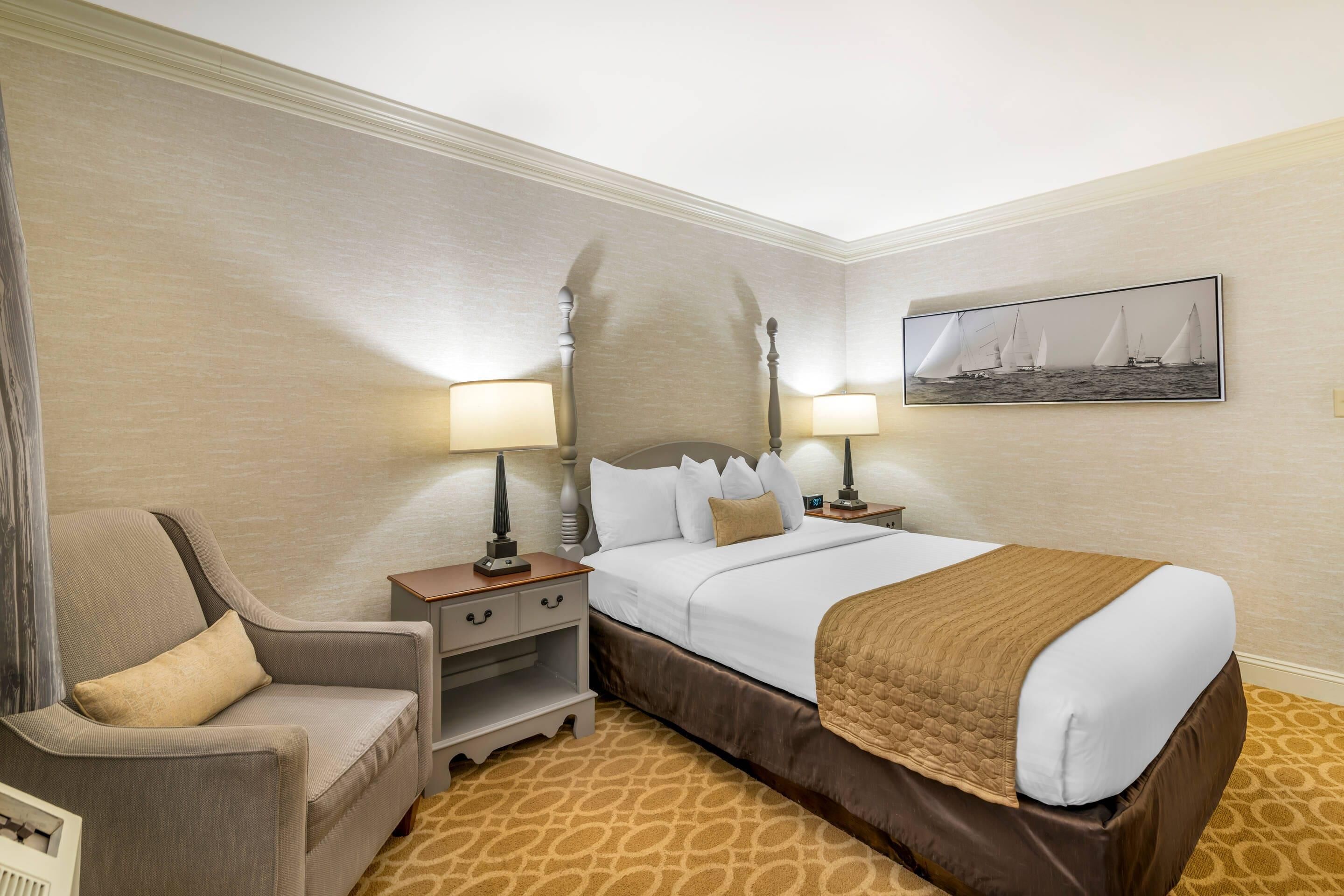 A hotel room with a bed, two bedside tables, a chair, a nightstand, and a wall-mounted picture.