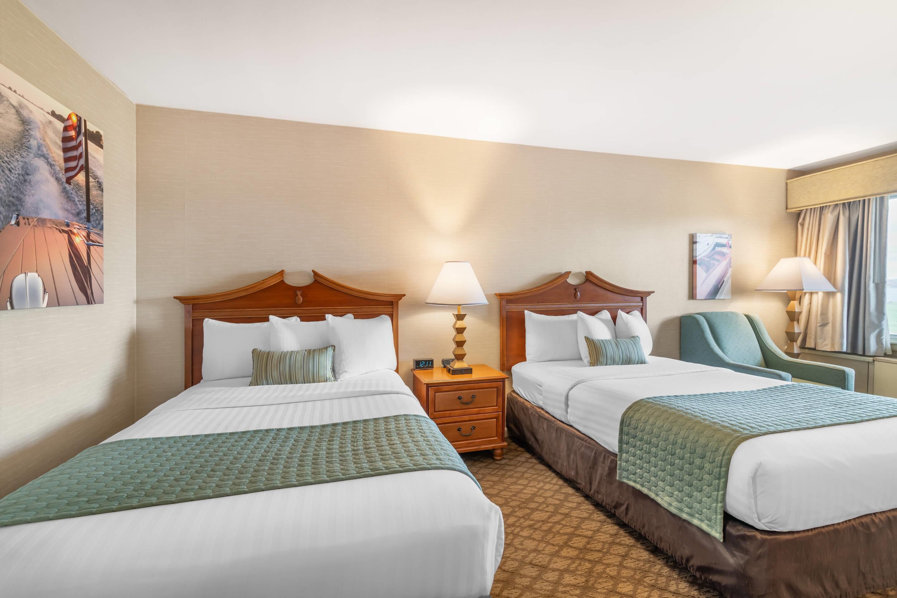 Une chambre d’hôtel avec deux lits, une table de chevet, une lampe, une chaise et un tableau au mur.