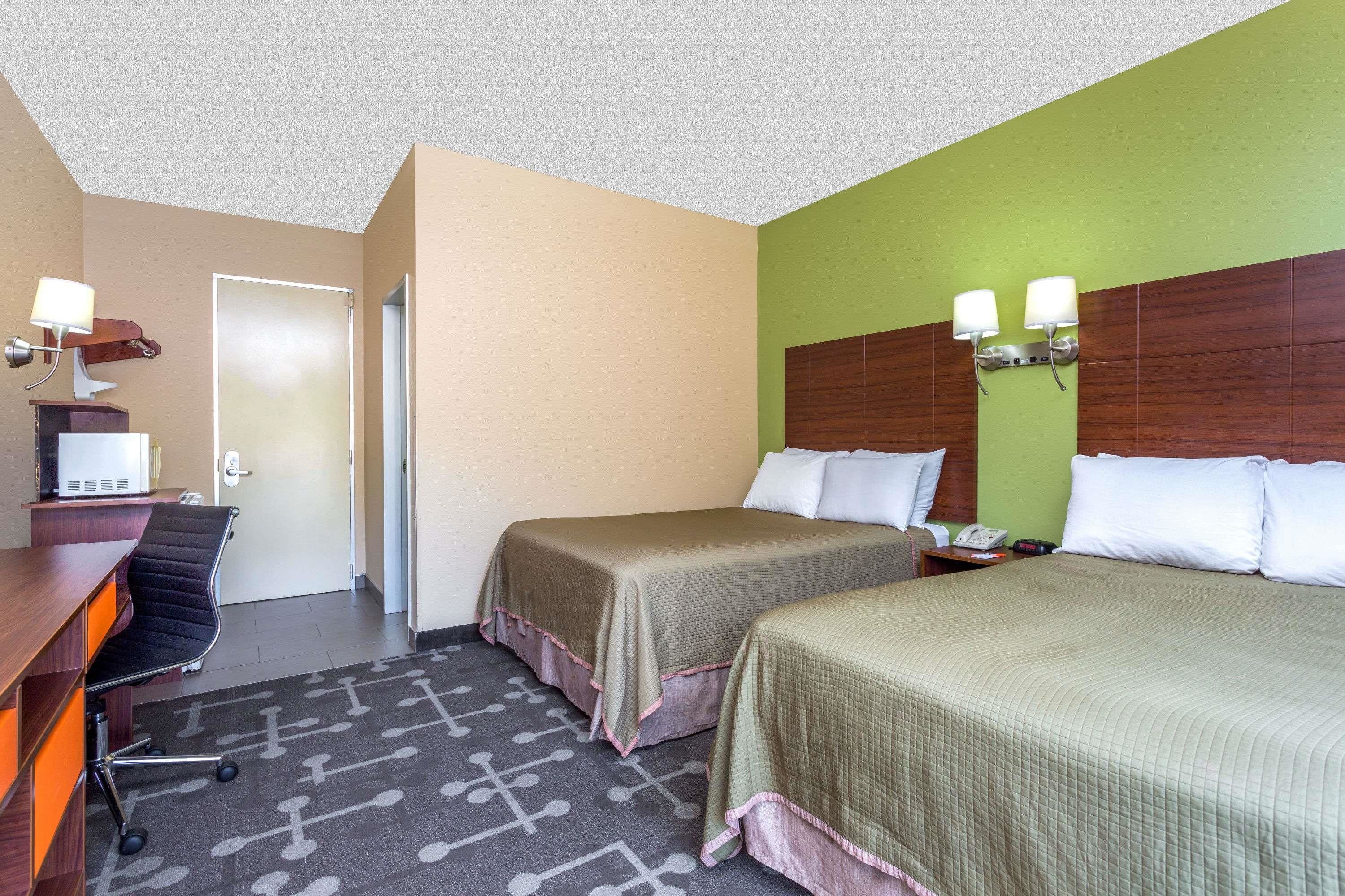 A hotel room with two beds, a desk with a chair, a telephone, and a wall-mounted light fixture.