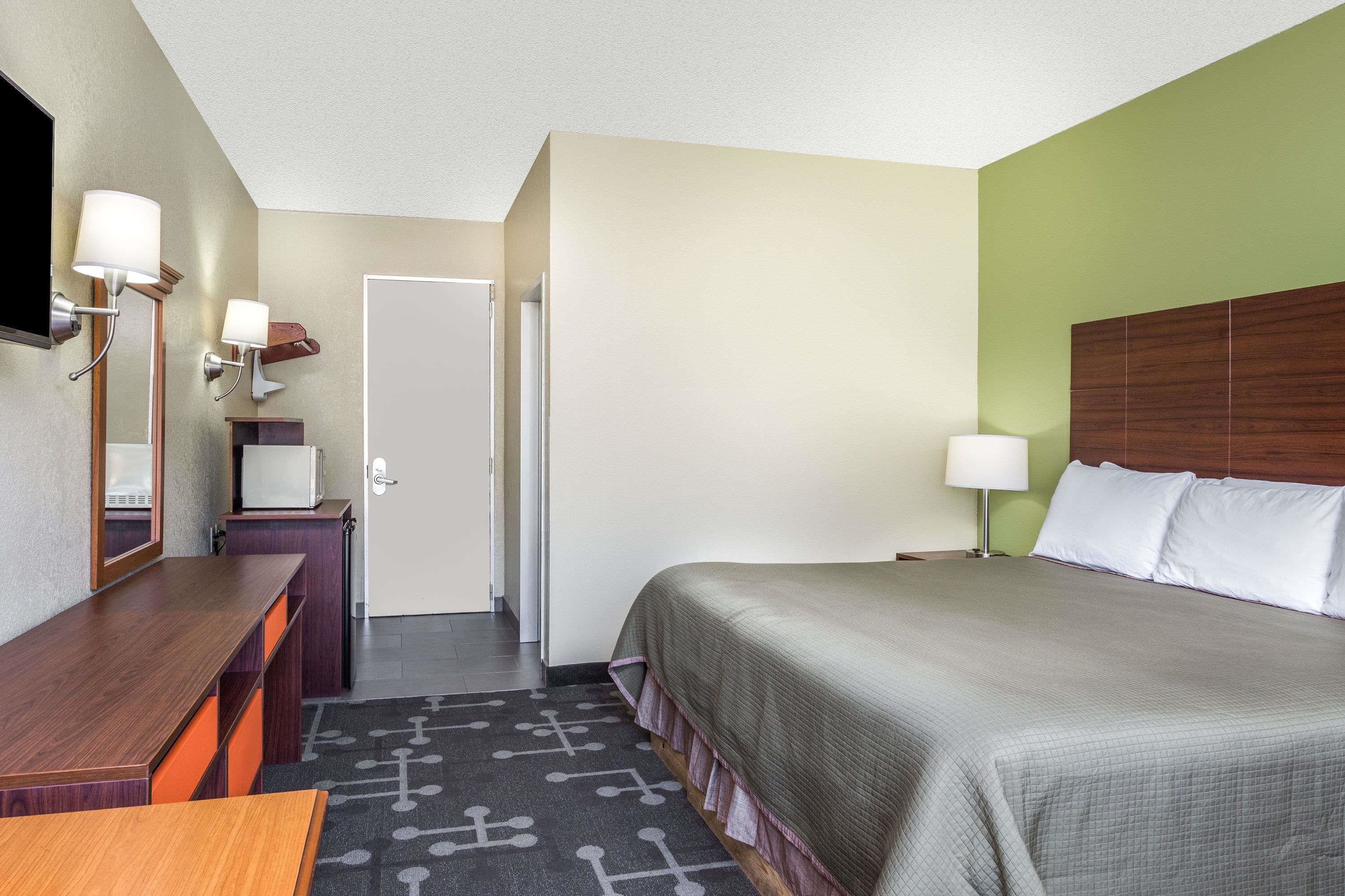 Una habitación de hotel con cama, escritorio, silla, televisor y puerta.