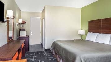 A hotel room with a bed, a desk, a chair, a TV, and a door.