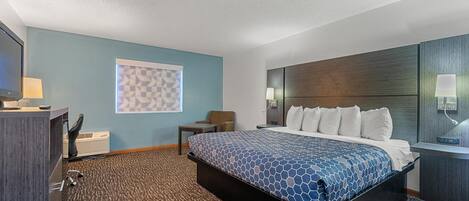 A hotel room with a large bed, a desk with a lamp, a TV, and a wall-mounted light.