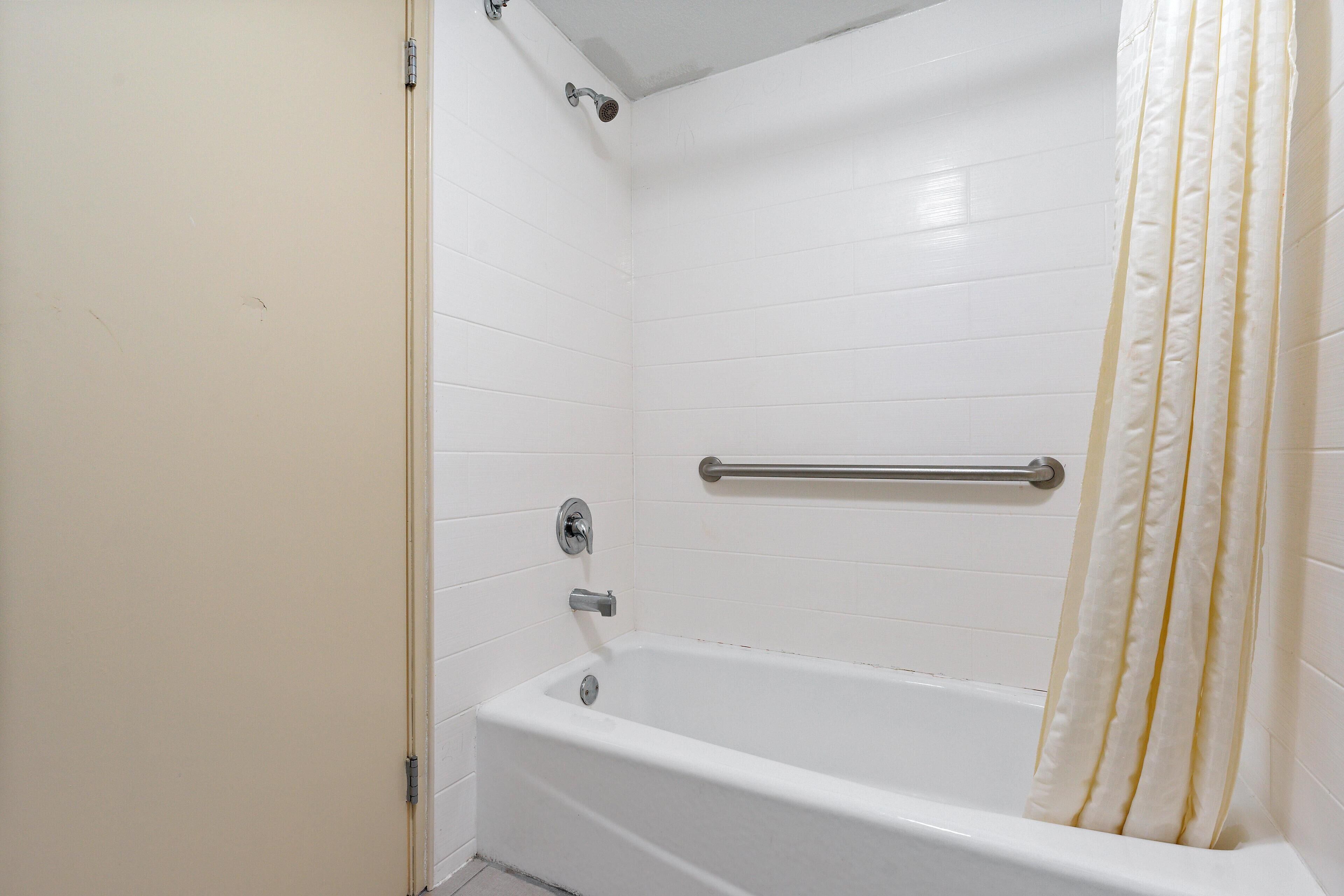 Ein schlichtes, weißes Badezimmer mit Badewanne, einer Haltestange und einer Duschvorhang.