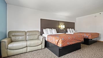 A hotel room with a sofa, a double bed with patterned bedding, and a headboard with wall-mounted lights.