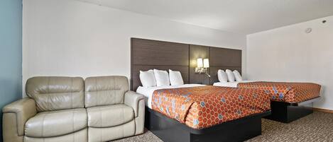 A hotel room with a sofa, a double bed with patterned bedding, and a headboard with wall-mounted lights.