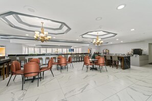 A modern hotel lobby with a central bar, seating area with chairs, and a marble floor.