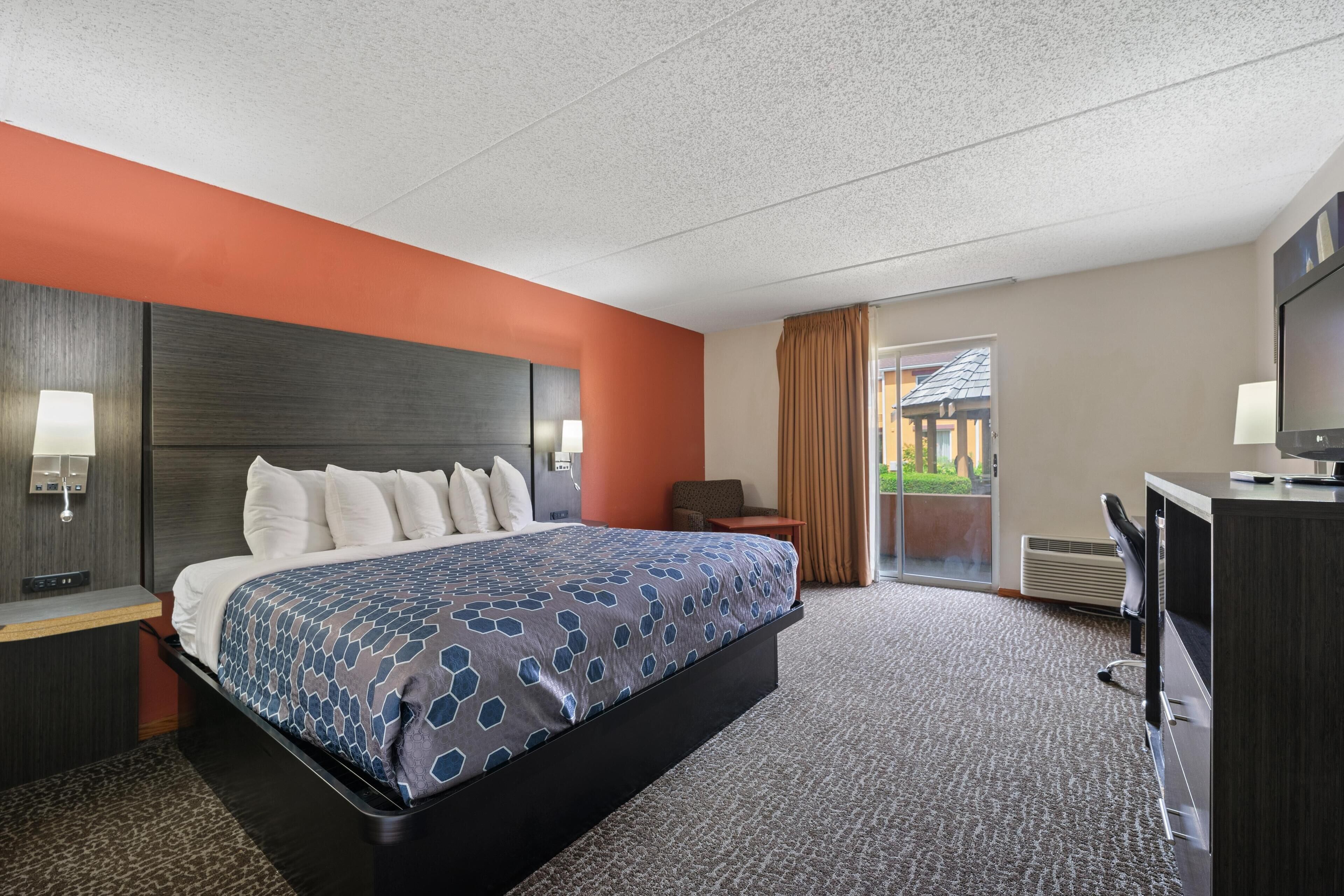 A hotel room with a large bed, a desk with a computer, a TV, and a view of the outdoors through a sliding door.