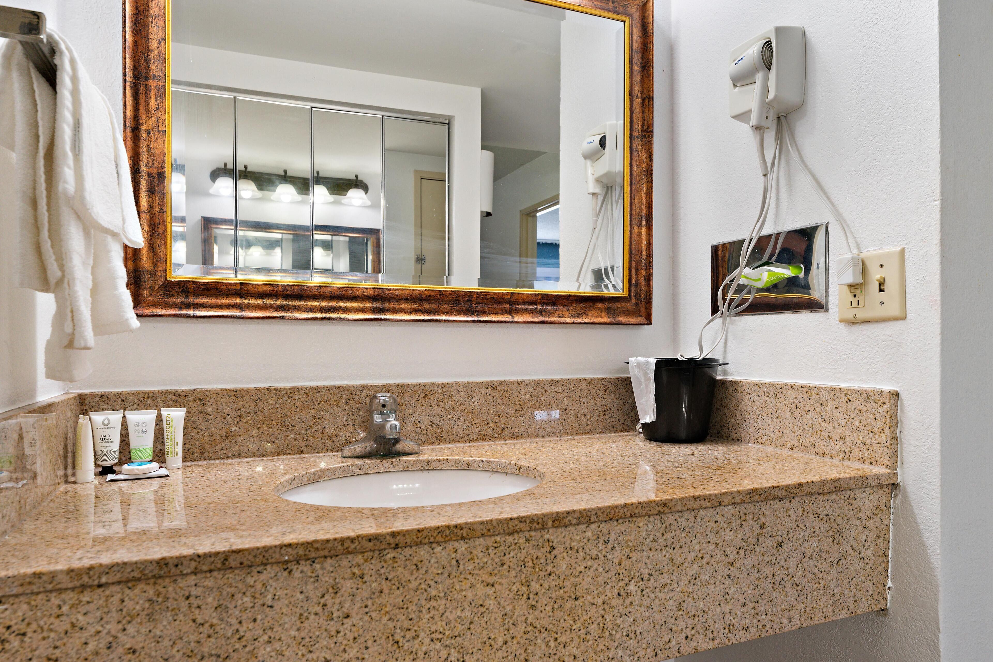 Un baño con encimera de granito, un lavabo, un espejo y un perchero para toallas.