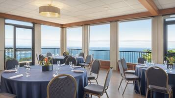 Un comedor con mesas y sillas redondas, ventanas amplias con vista al mar e iluminación empotrada en el techo.