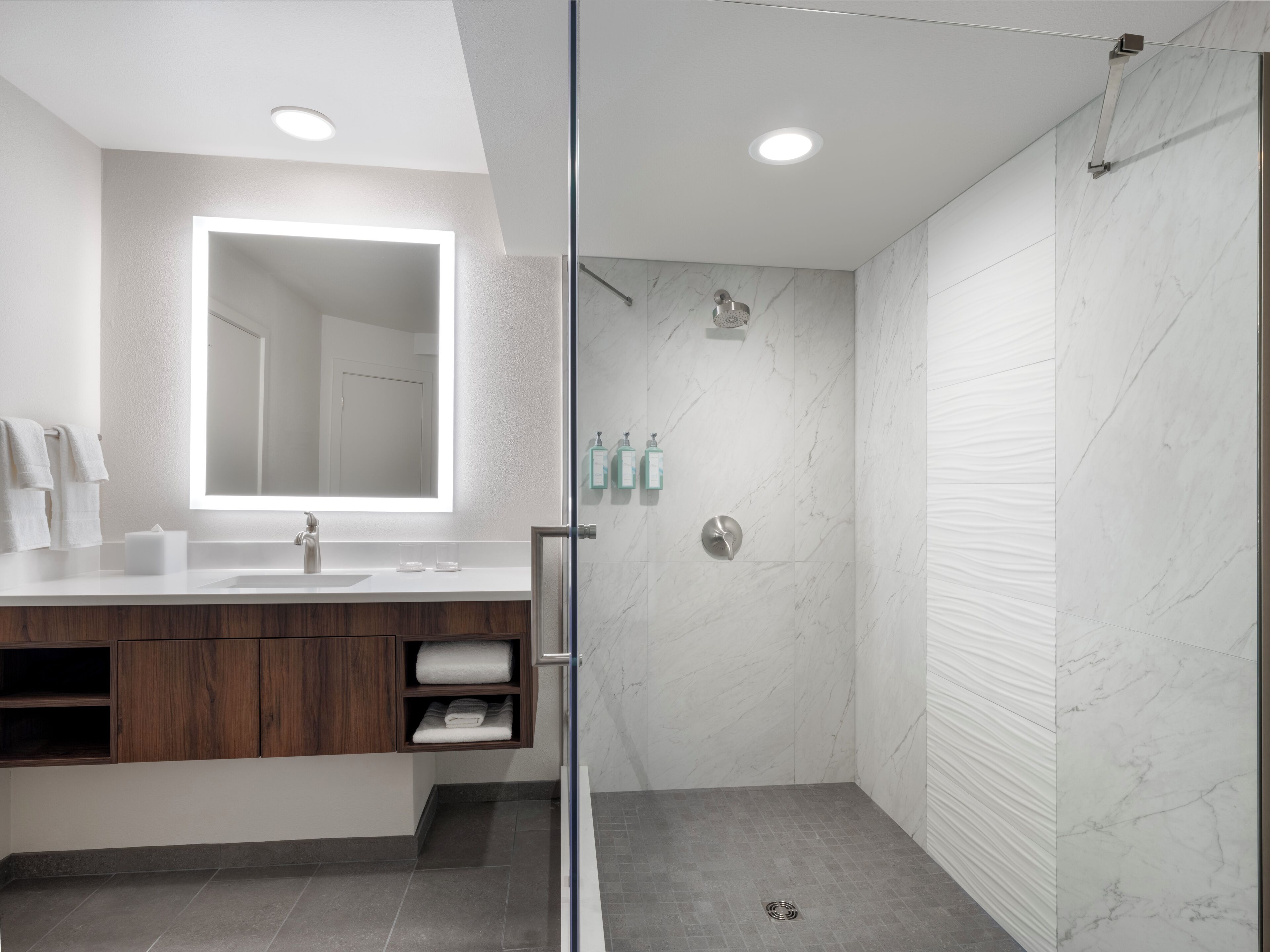 A modern bathroom with a glass shower enclosure, a large mirror, and a wooden vanity.