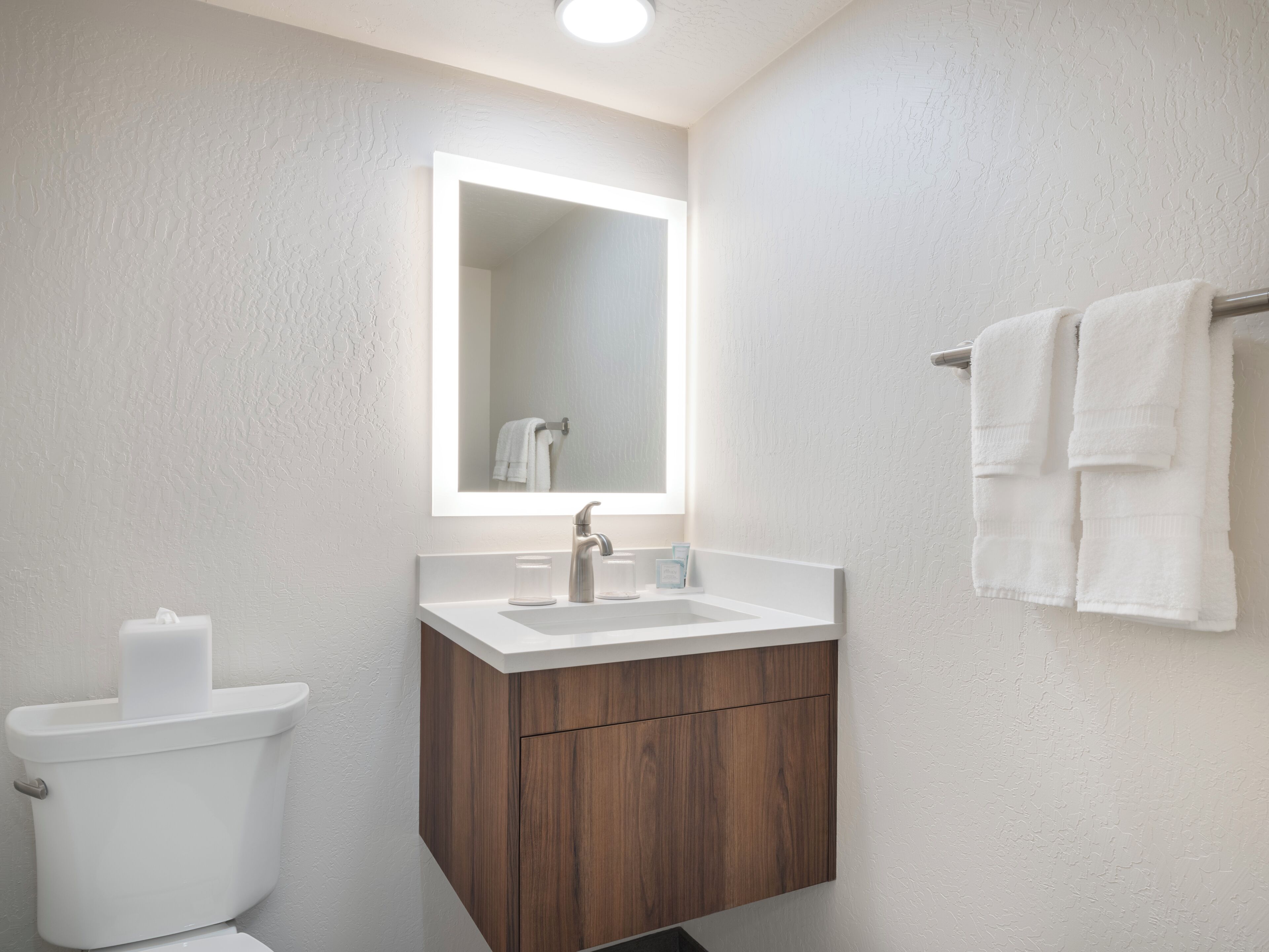 A modern bathroom with a white sink, wooden vanity, and a toilet.
