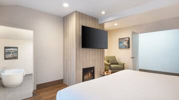 Una habitación de hotel moderna con una cama grande, un televisor de pantalla plana en la pared, una chimenea, un sillón verde y un baño con bañera y lavamanos.