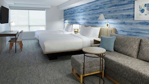 A hotel room with a large bed, a sofa, a desk, and a chair. There is a window providing a view of the city. - TownePlace Suites by Marriott Niagara Falls Canada (Niagara Falls)