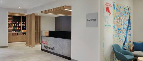 A reception area with a counter labeled "HELLO Niagara Falls," a map on the wall, and seating with a rug.