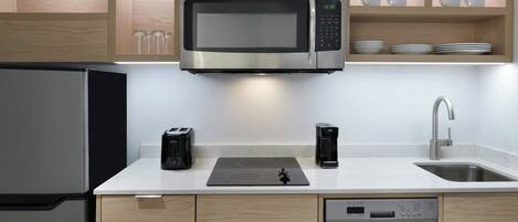 A modern kitchen with a built-in microwave, toaster, and coffee maker on the countertop, a dishwasher, and wooden cabinetry.