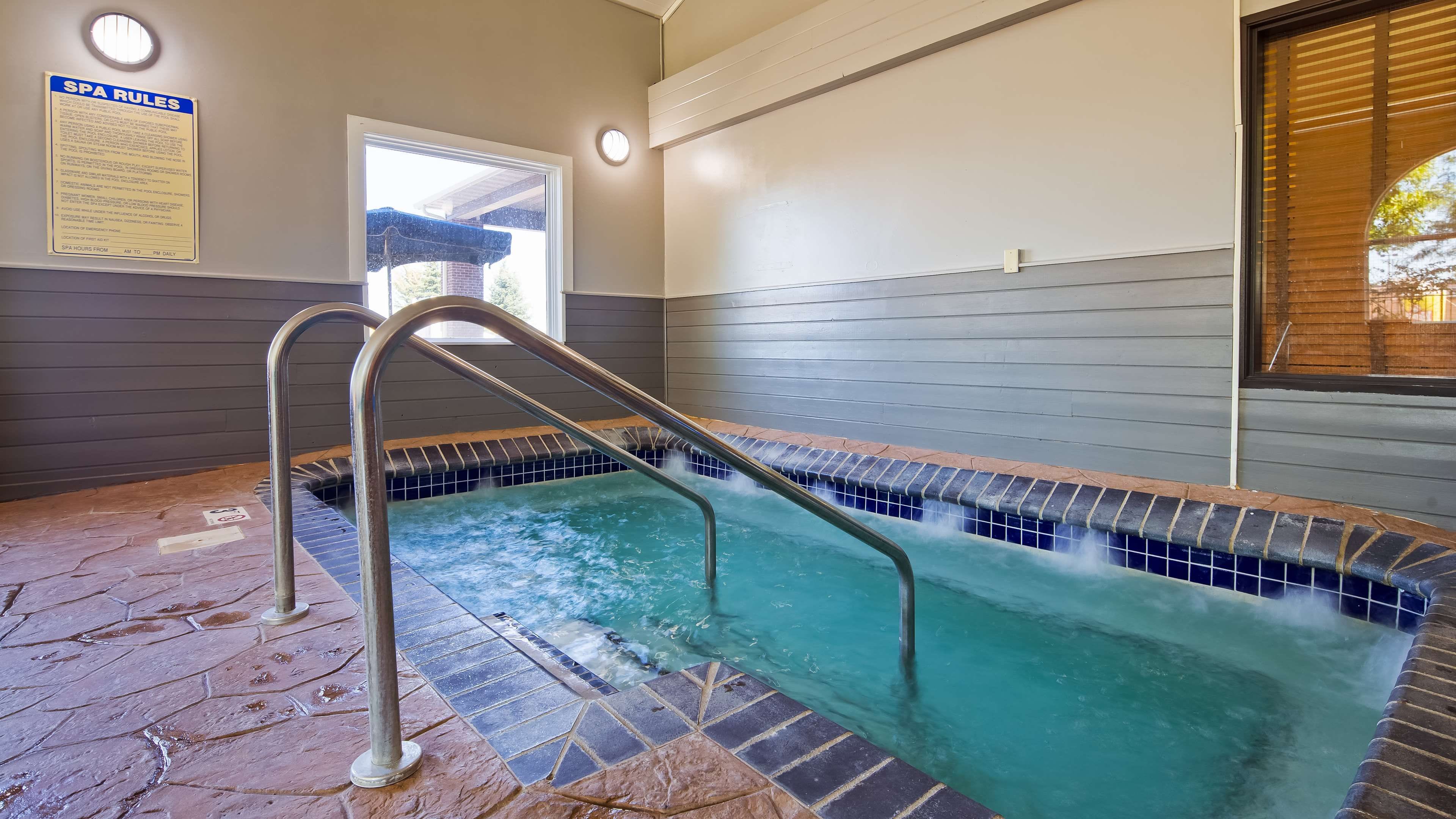 Un jacuzzi con una escalera metálica, piso de baldosas y un cartel con las normas del spa.