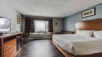 Ett hotellrum med en säng i trä, ett skrivbord med en stol, en tv och ett fönster med gardiner.