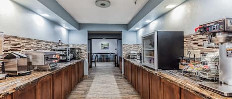A long, narrow commercial kitchen with stainless steel appliances and a tiled backsplash.