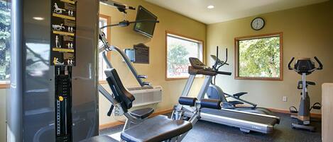 Un gimnasio con cintas de correr, máquinas de pesas y un televisor instalado en la pared.