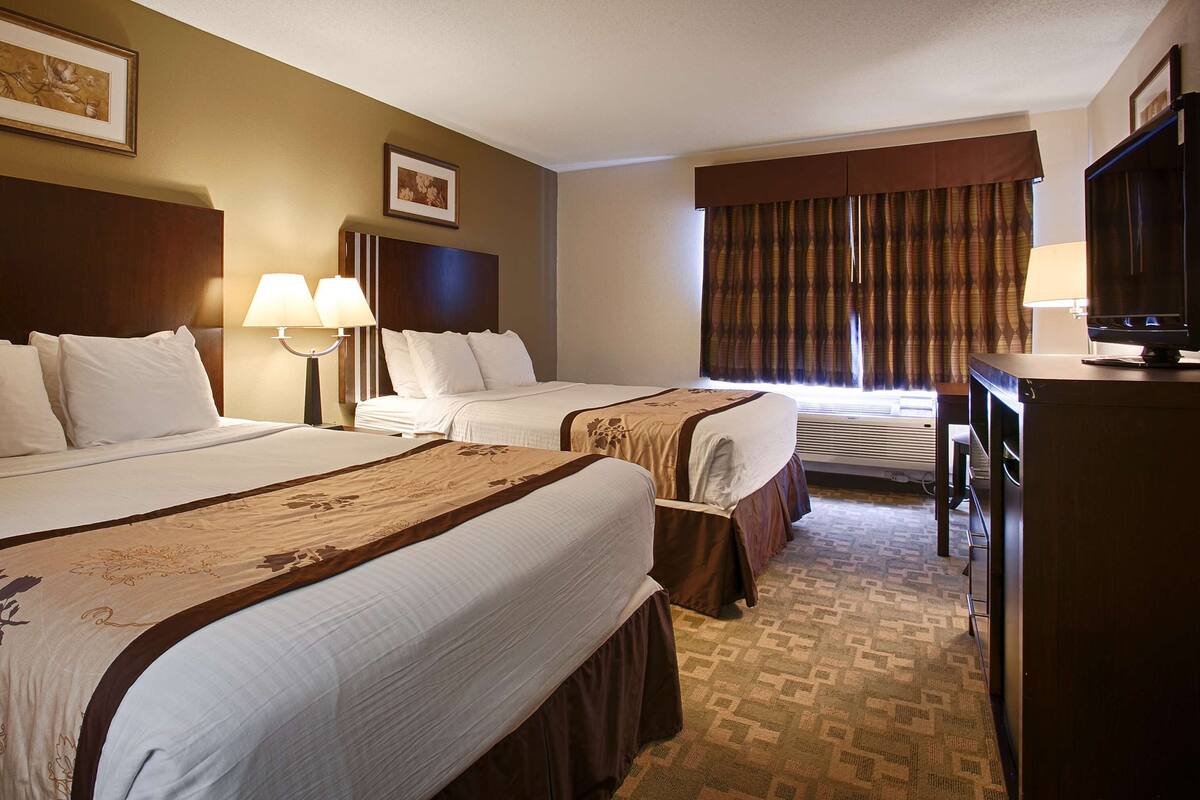 A hotel room with two beds, a television, and a window with curtains.