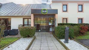 A B&B hotel entrance with a modern design, including a glass door, a sign above the entrance, and a pathway leading to the door. - B&B HOTEL Blois Nord Vallee Maillard (Blois)