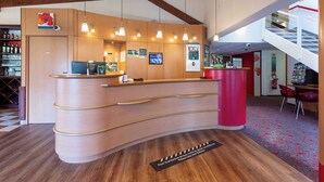A reception desk with a wooden finish, overhead pendant lighting, and a red accent wall. - B&B HOTEL Blois Nord Vallee Maillard (Blois)