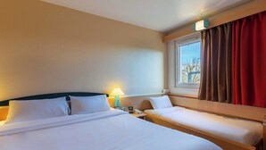 A hotel room with a large bed, a smaller bed, a window with curtains, a lamp, and a bedside table. - B&B HOTEL Blois Nord Vallee Maillard (Blois)