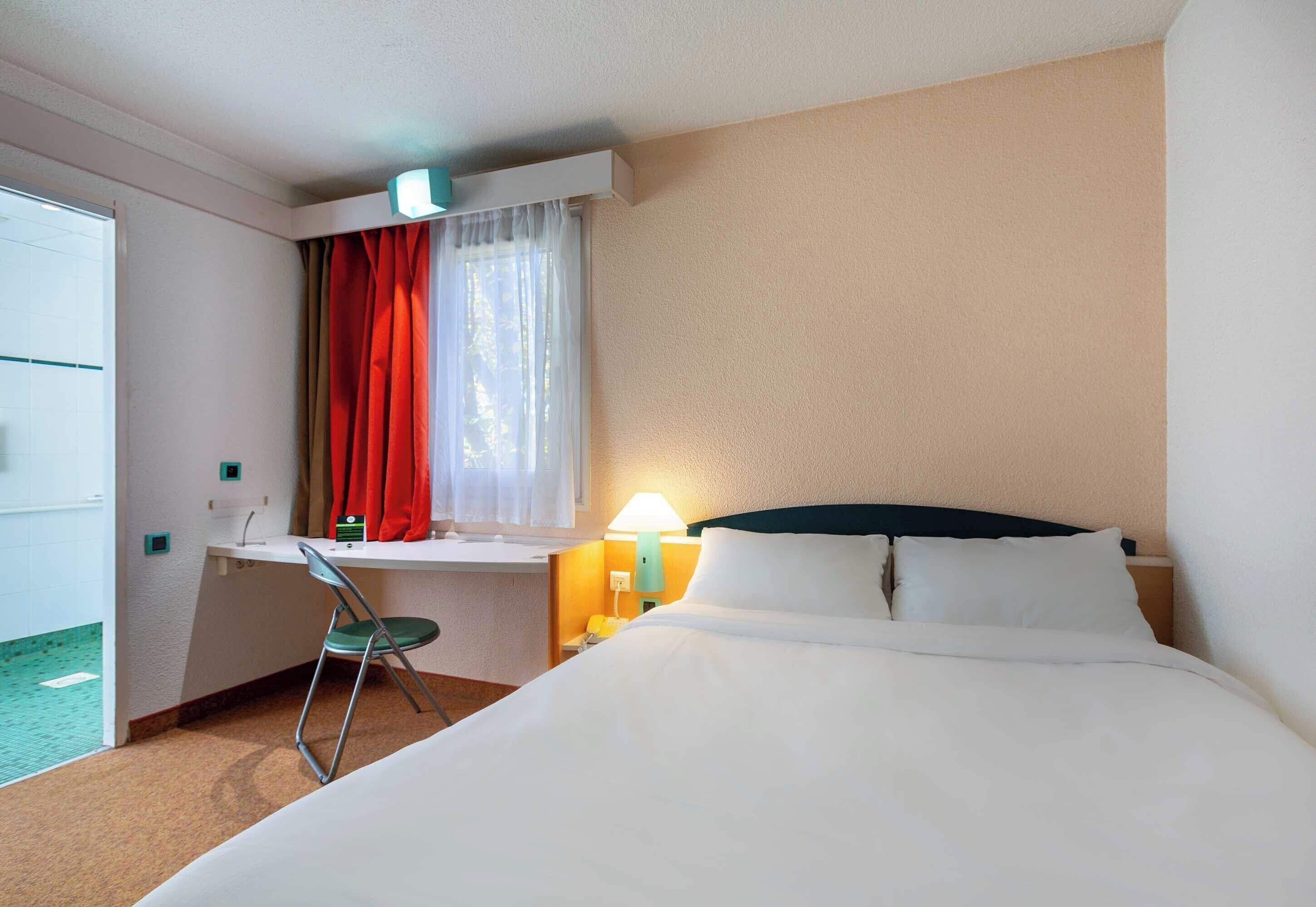 Een hotelkamer met een bed, bureau, stoel en een raam met gordijnen.